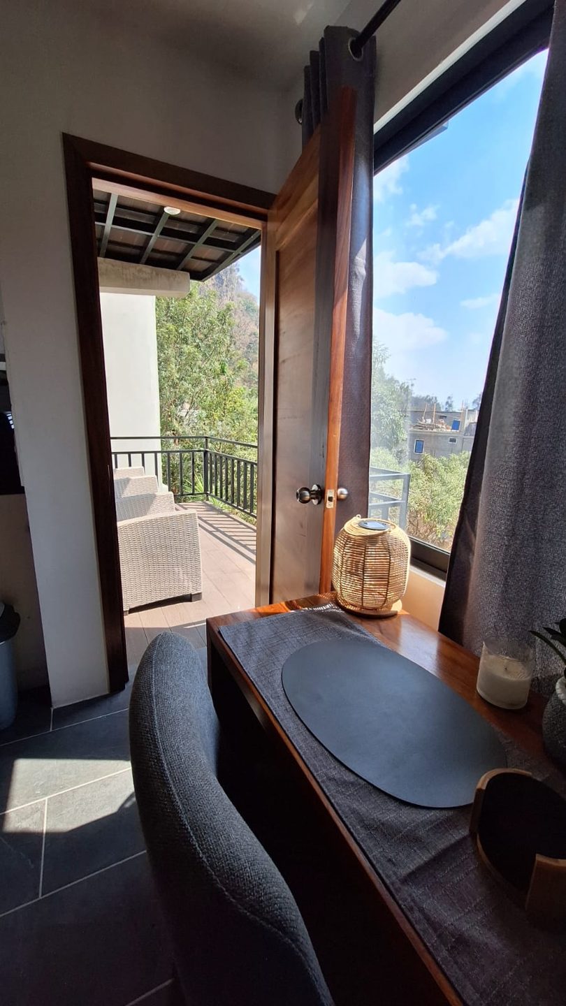 La mesa junto a la ventana, con la puerta del balcón abierta hacia los árboles